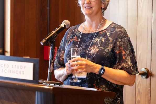 A person with a champagne flute speaks from the podium.