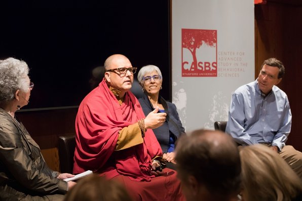 Buddhist monk speaking as the other three presenters listen.