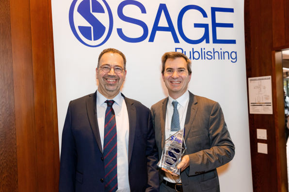 Daron Acemoglu & Sage representative Doug McCune posing in front of a Sage retractable banner 