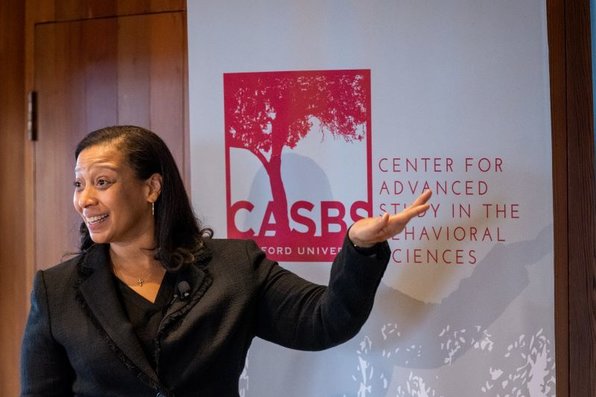 Jennifer Richeson gestures, standing in front of a CASBS poster.