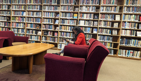 2025-26 fellow Nasandratra Ravonjiarison is reading a Tyler book while the Tyler Collection looms behind her.