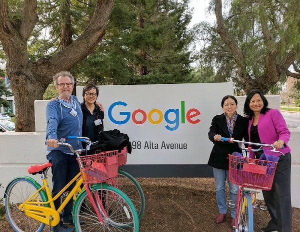 Four people pose in front of a Google building sign with some Google bikes