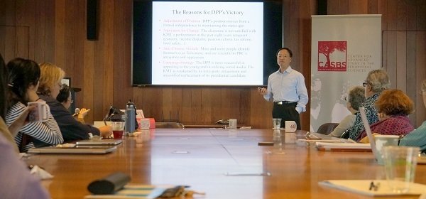 Jiang standing in front of his slides as he addresses the conference room table full of participants.