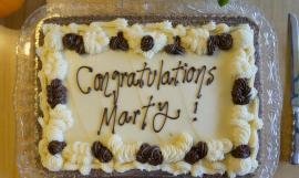 A decorated cake reading “Congratulations Marty” in icing