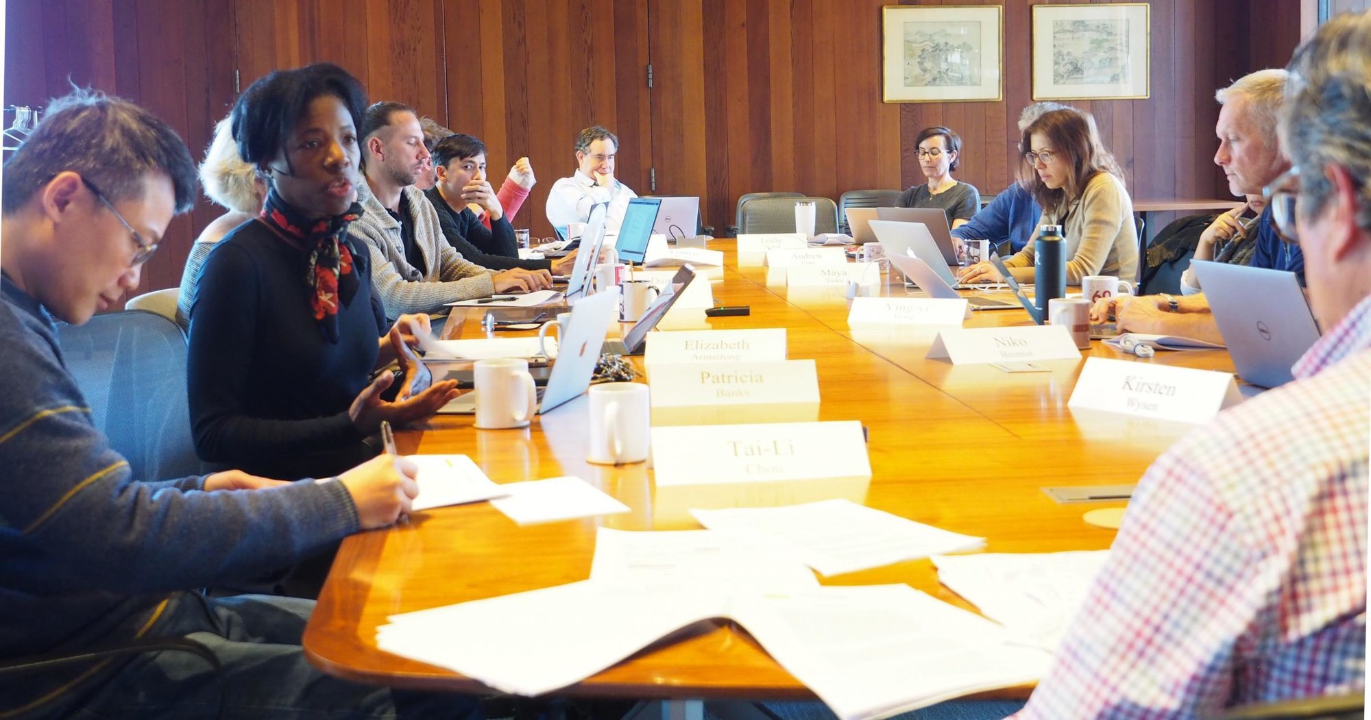 a diverse group of people sitting at a conference table with papers spread out and conversations going