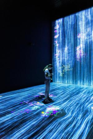a young woman stands as a light installation projects streams of blue-white light flowing around her