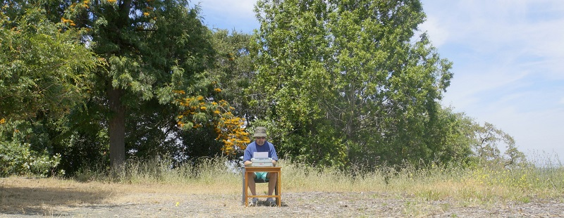 Front view of Frank using a typewriter while sitting in a desk in the middle of nowhere